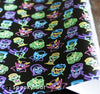 Close-up of black gift wrap paper printed with colorful neon line-art portraits of classic monsters, including Frankenstein, Dracula, Wolfman, Creature from the Black Lagoon, and the Bride of Frankenstein. Bright 80s aesthetic on a dark background.