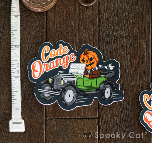 Diecut vinyl sticker of a jack-o'-lantern-headed figure driving a green vintage car with the words “Code Orange.”