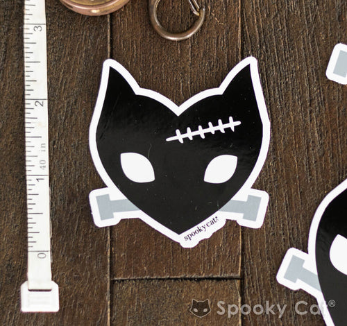 Diecut vinyl sticker of a black cat face with stitch detail and gray bolts inspired by Frankenstein’s monster.